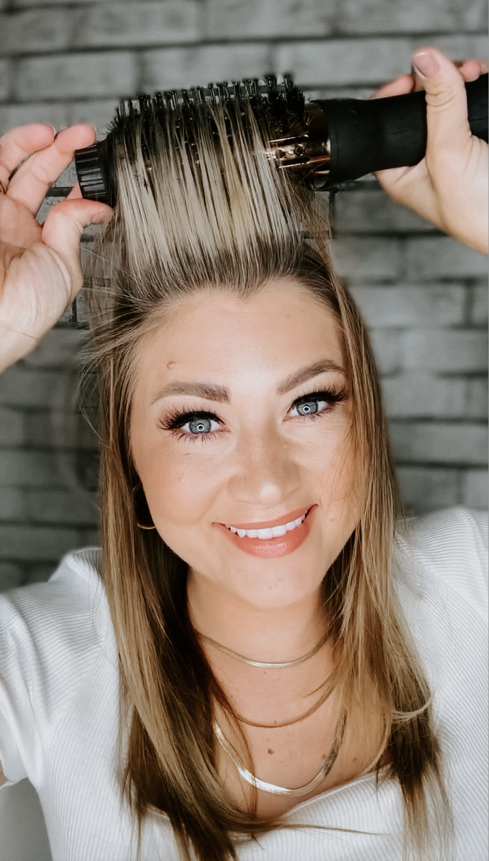 Savannah Kreger lifting the top section of her blonde hair with a large round L’ange styling brush while creating volume and a smooth blowout look