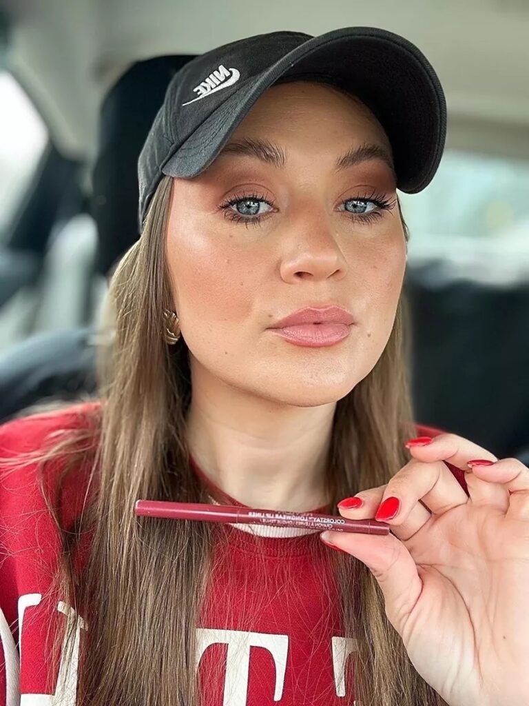 thesavannahk wearing casual red sweatshirt and black Nike hat, showing drugstore lip liner with soft glam makeup look