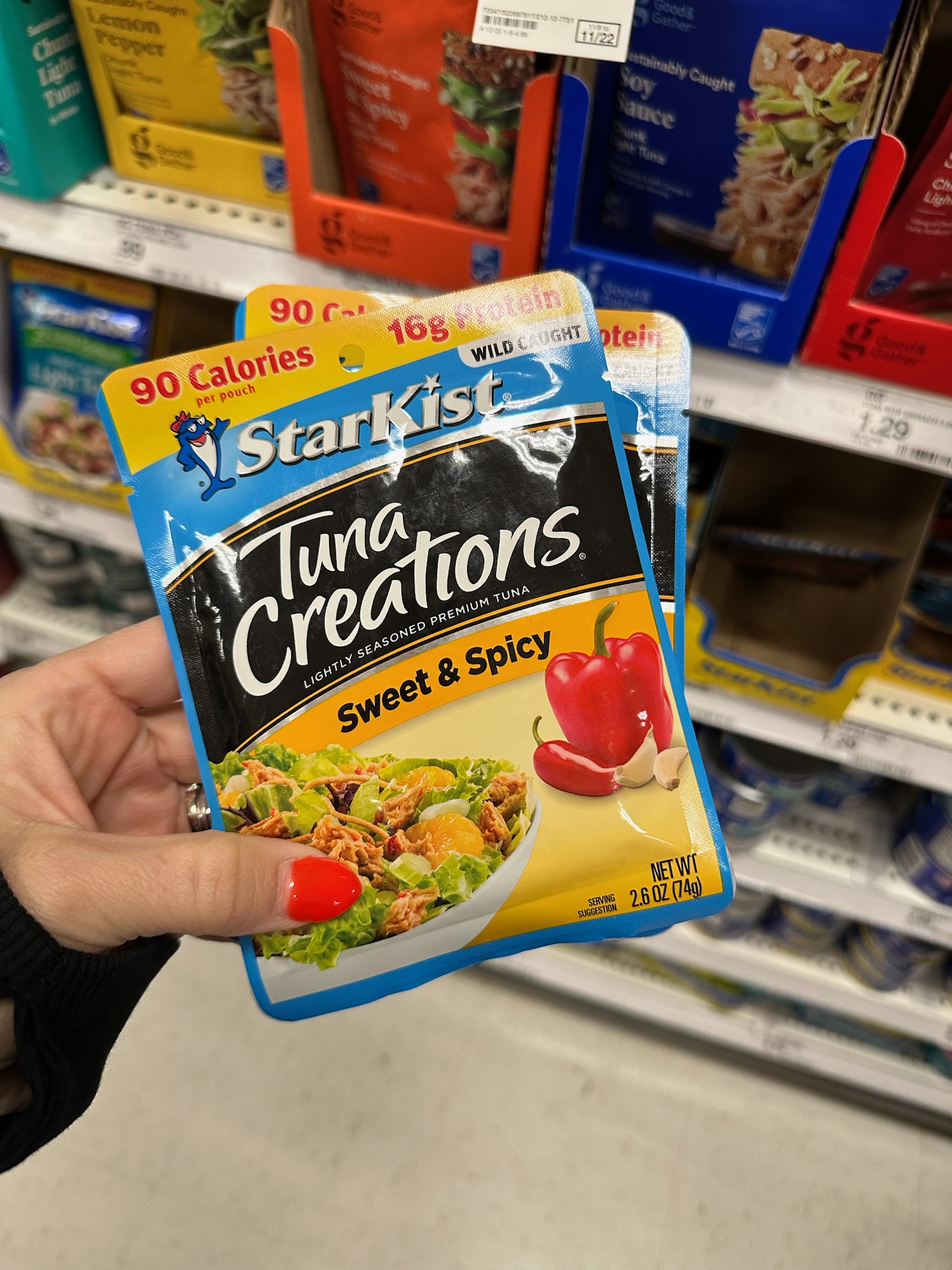 A hand holding a pouch of StarKist Tuna Creations Sweet and Spicy flavor in a grocery store aisle.