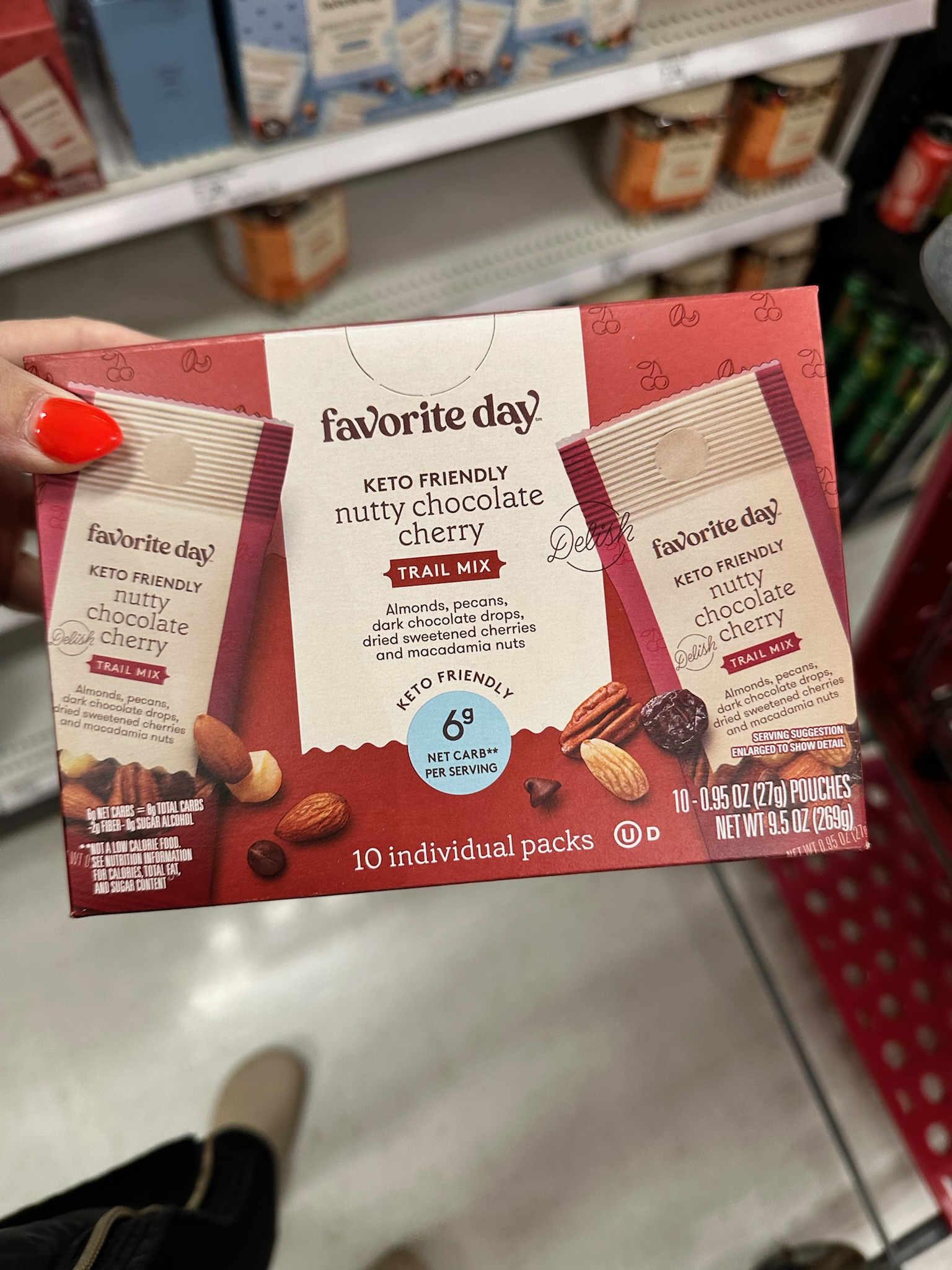 A hand holding a box of Favorite Day keto friendly nutty chocolate cherry trail mix packets at Target.