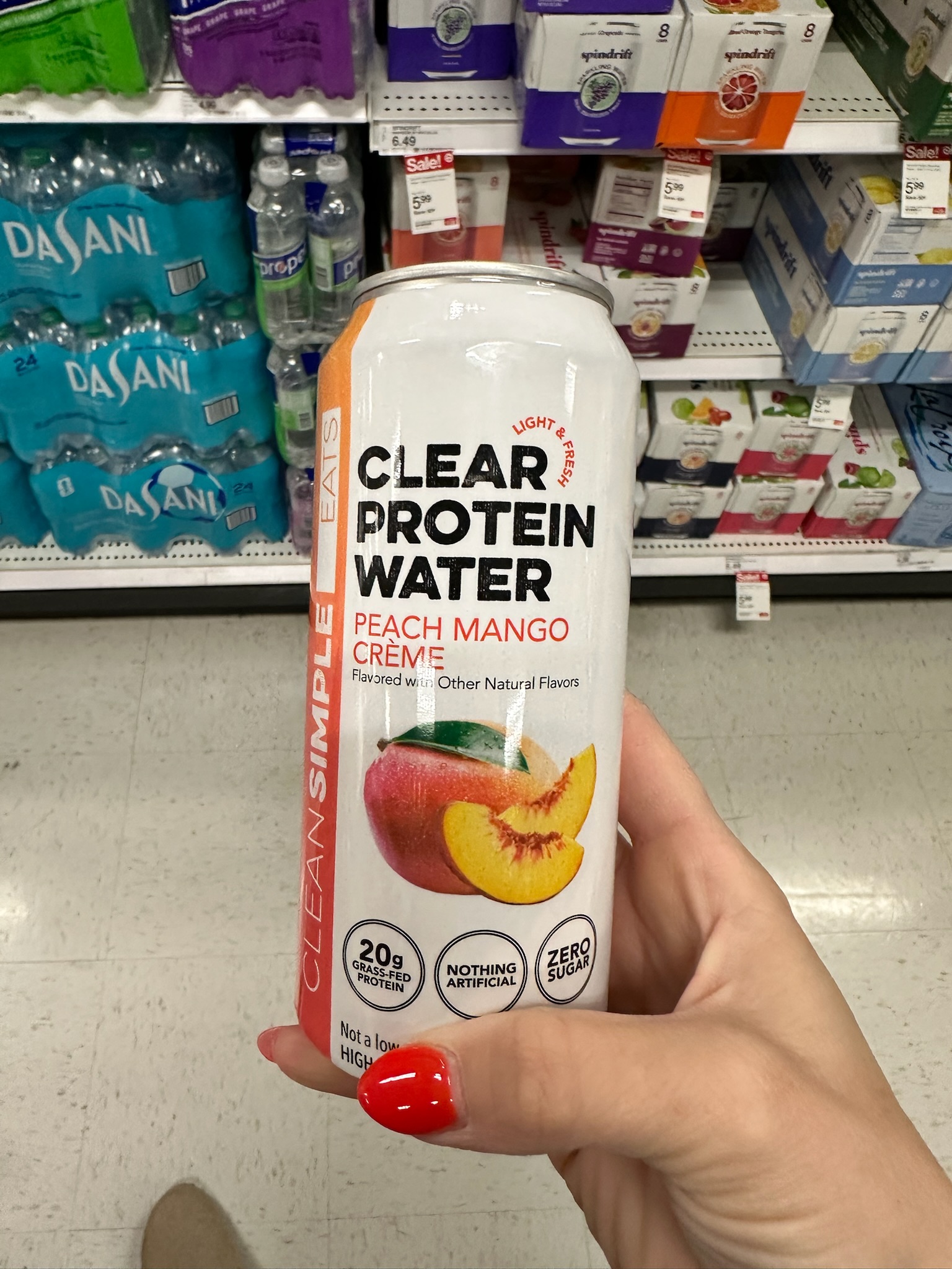 A hand holding a can of Clear Protein Water in peach mango crème flavor in the beverage aisle at Target.