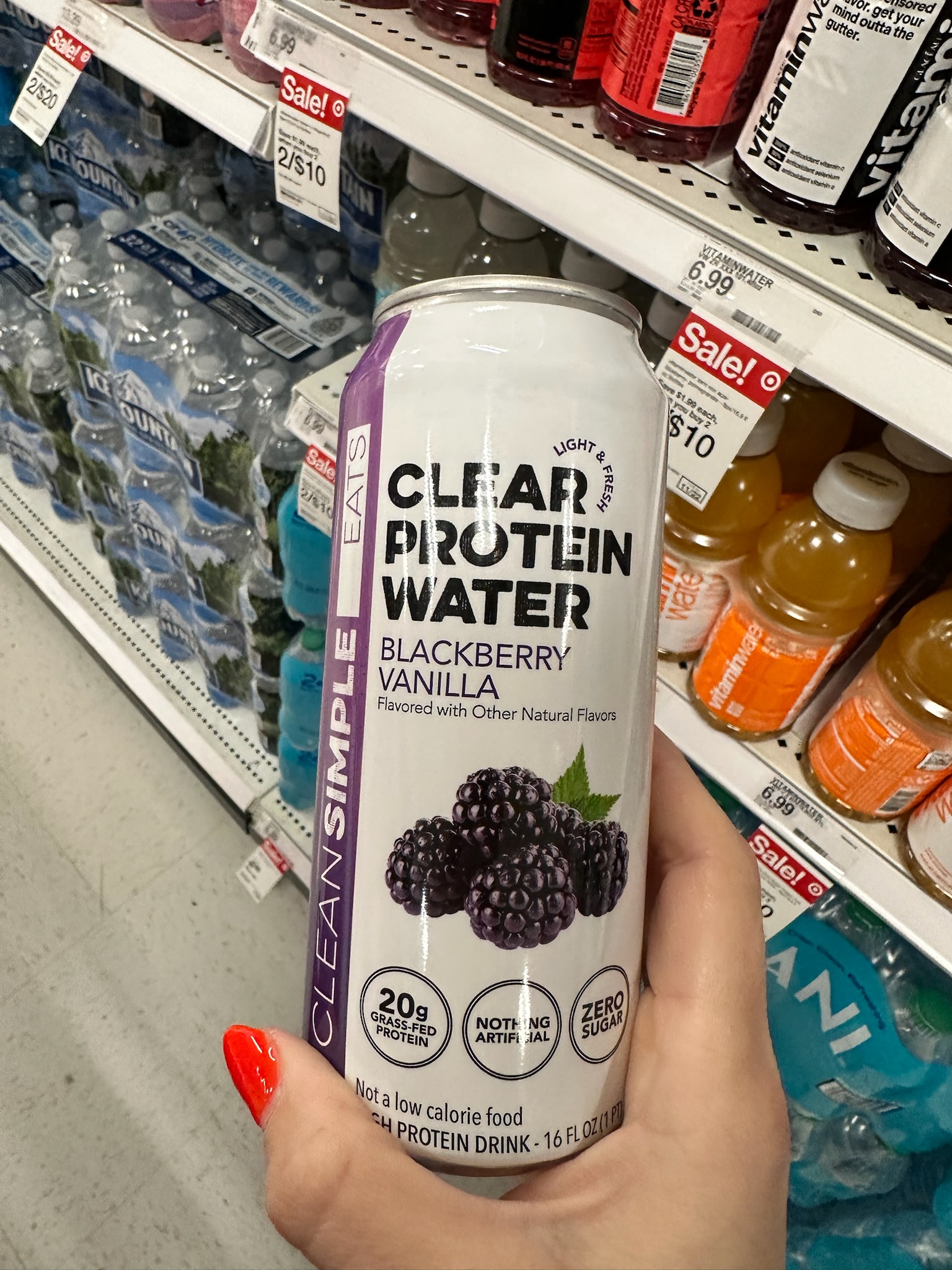A hand holding a can of Clear Protein Water in blackberry vanilla flavor in the drink aisle at Target.