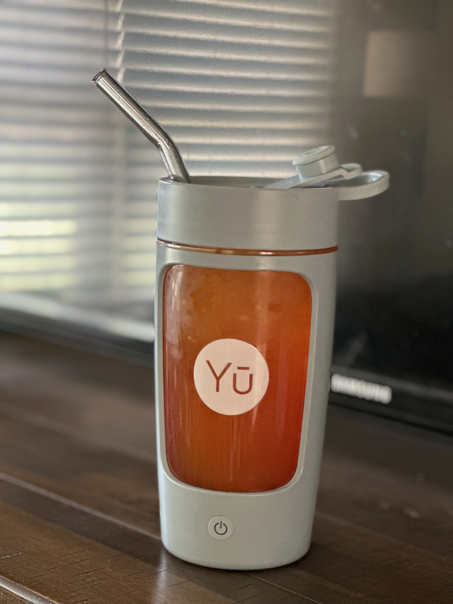 A Yu Supplements water bottle with a metal straw filled with a reddish drink sitting on a wooden surface.