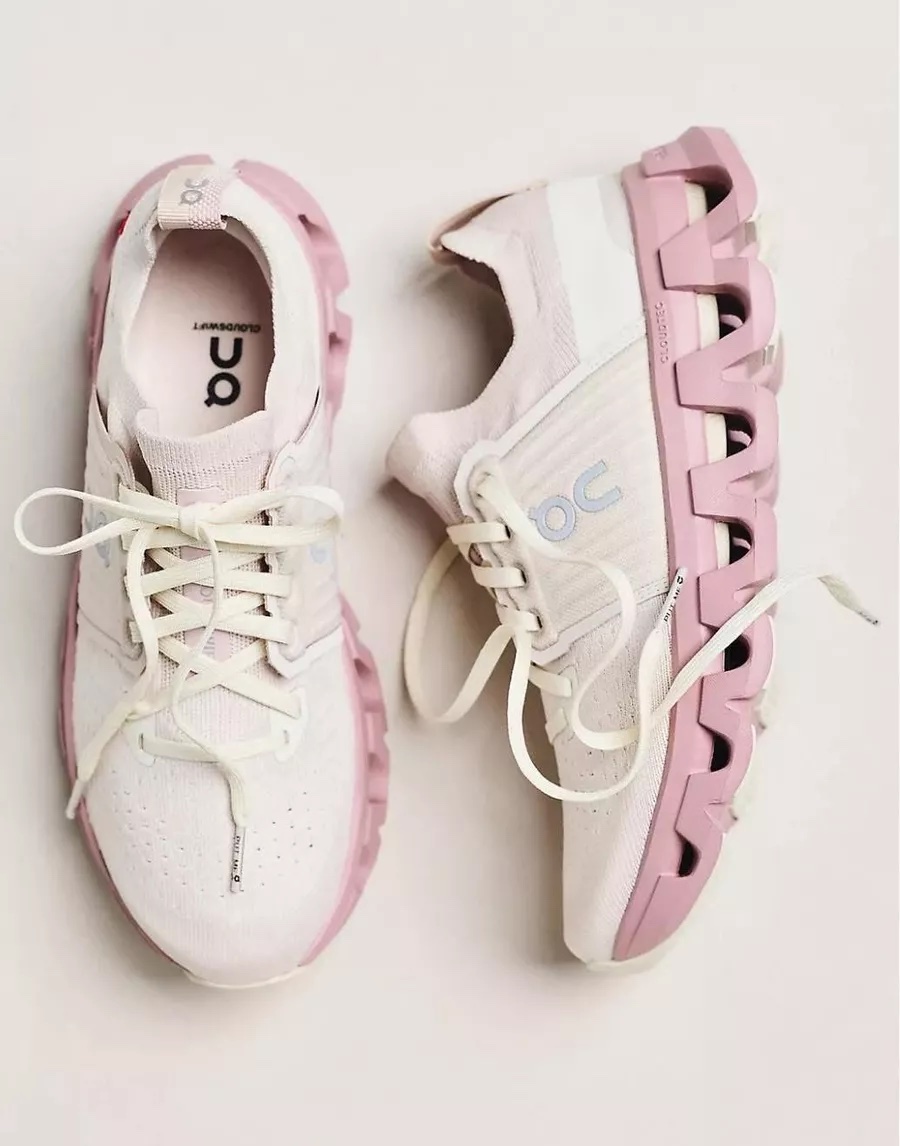 A pair of light pink and white On Cloud running shoes displayed on a neutral background.