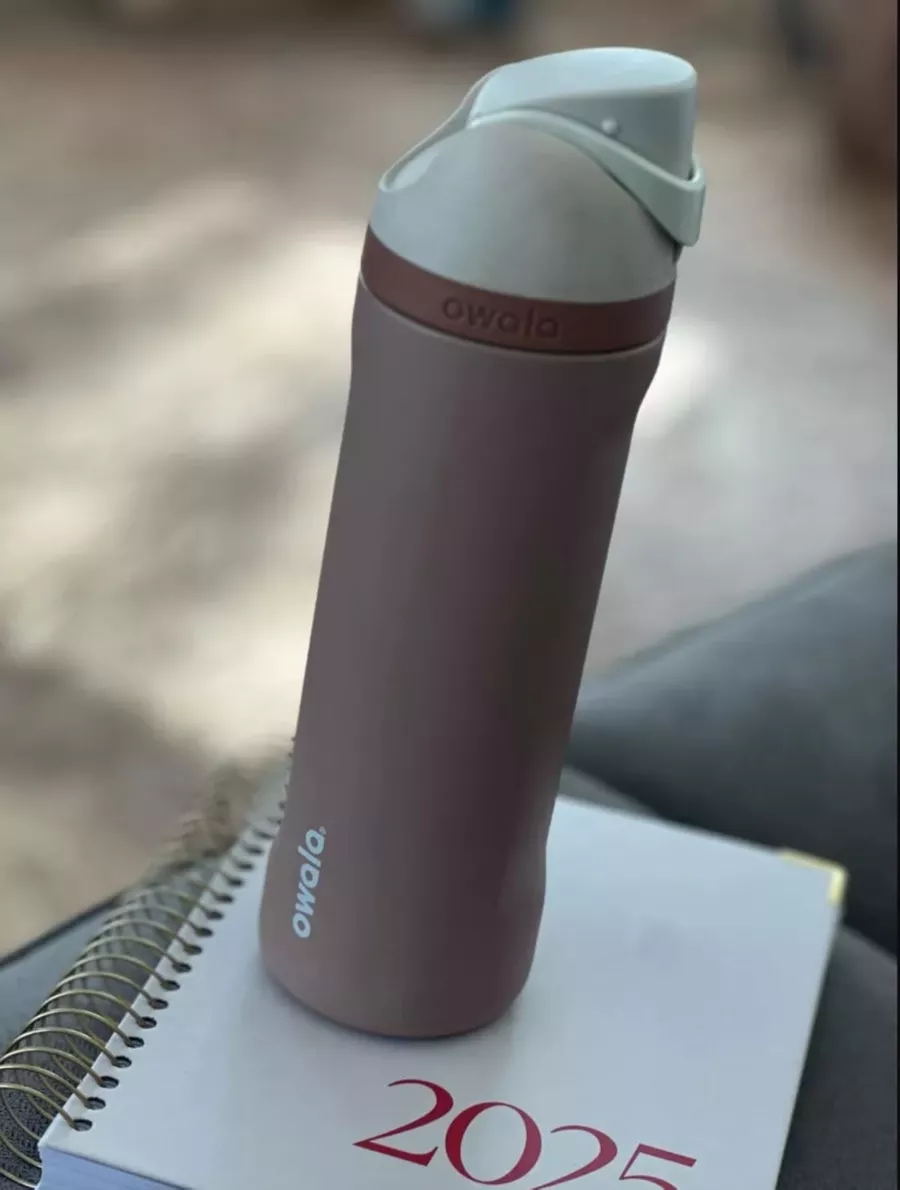 A mauve Owala water bottle resting on top of a 2025 planner with soft natural light in the background.